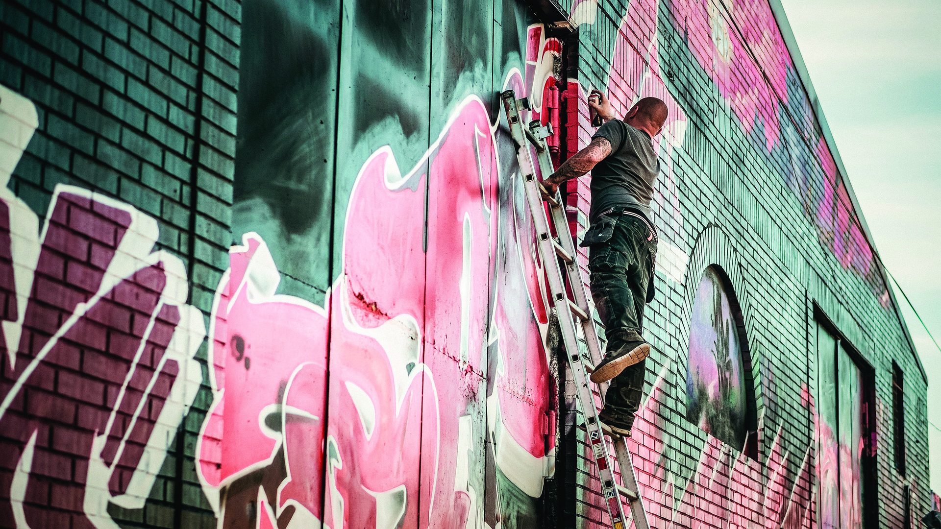 Instalador pintando un mural de gran formato sobre una fachada de ladrillo